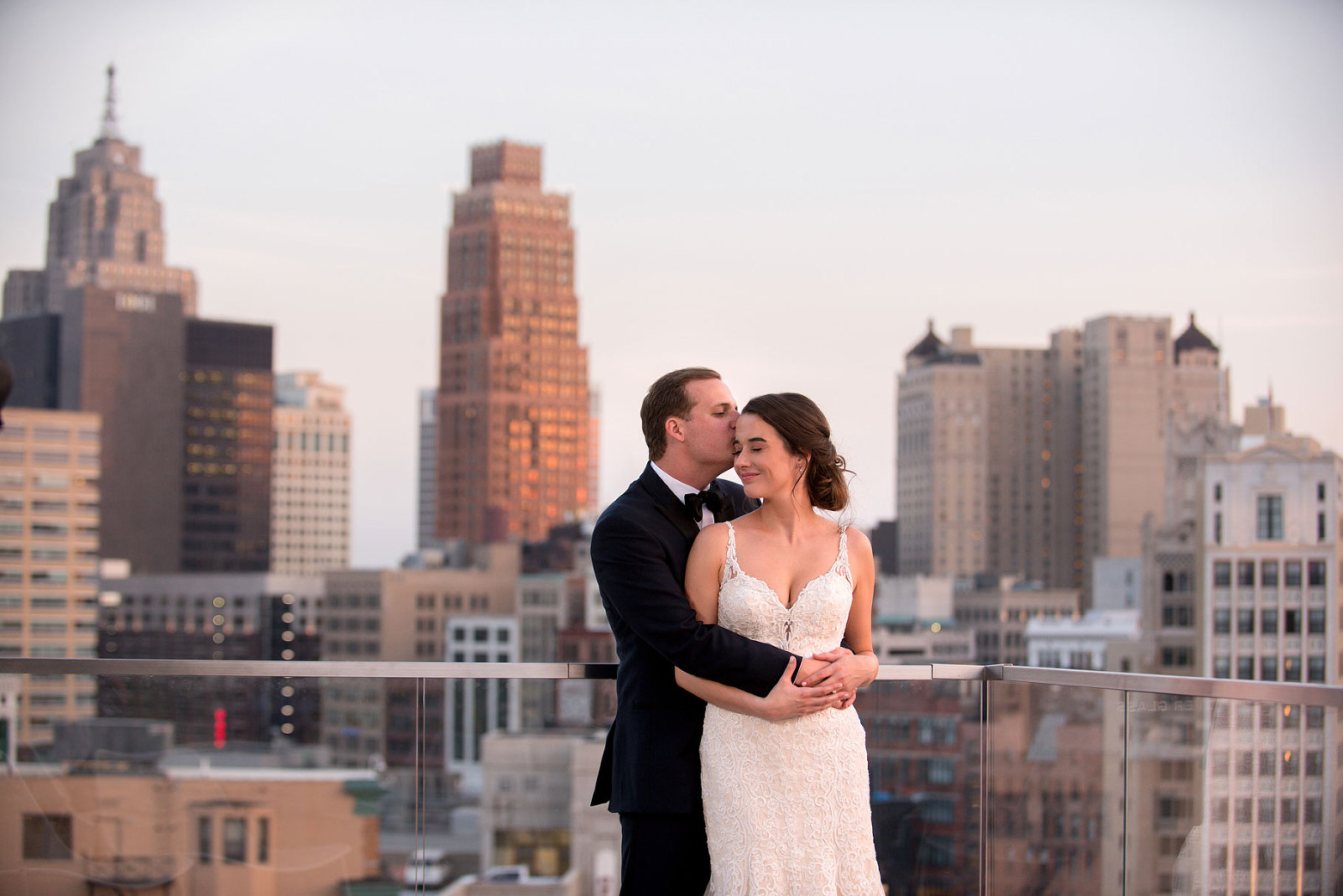 A bride and groom embrace on the balcony of the Detroit Athletic Club at sunset