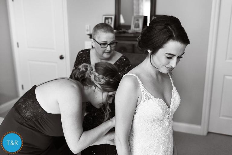 The maid of honor and mother of the bride, helping her into her dress