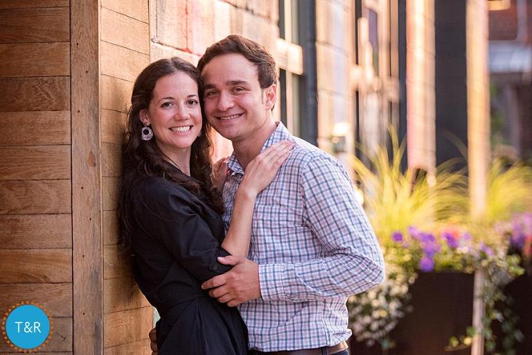 A couple is all smiles leaning against a wood wall