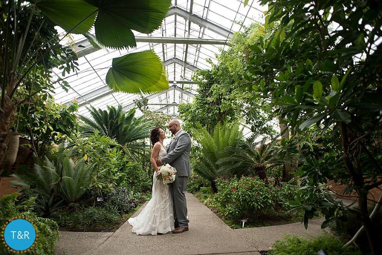 Bride and groom embrace at their Matthaei Botanical Gardens wedding, surrounded by tropical foliage