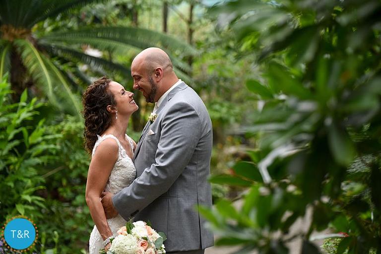 Bride and groom embrace at their Matthaei Botanical Gardens wedding, surrounded by tropical foliage